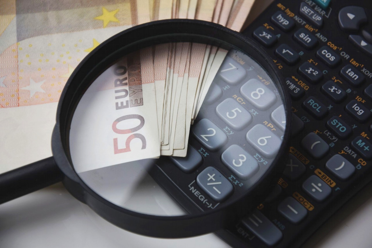 lente di ingrandimento su banconote e calcolatrice per focus su spese di registrazione contratto di locazione